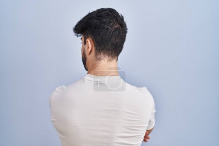 Foto de Hombre hispano con barba de pie sobre fondo blanco mirando hacia atrás con los brazos cruzados - Imagen libre de derechos
