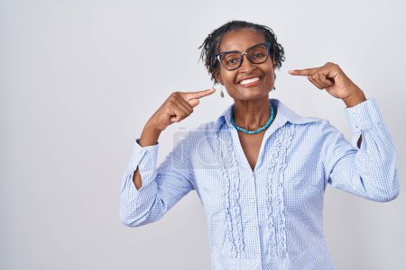 Téléchargez les photos : Femme africaine avec dreadlocks debout sur fond blanc portant des lunettes souriant gai montrant et pointant avec les doigts dents et la bouche. concept de santé dentaire. - en image libre de droit