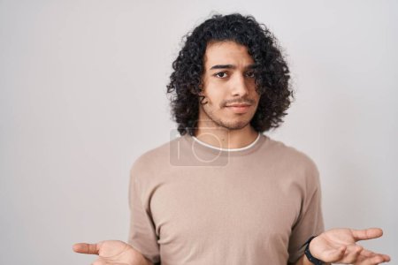 Photo for Hispanic man with curly hair standing over white background clueless and confused with open arms, no idea concept. - Royalty Free Image
