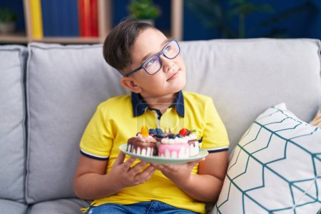Téléchargez les photos : Jeune enfant hispanique tenant bonbons gâteau souriant regardant vers le côté et regardant loin en pensant. - en image libre de droit