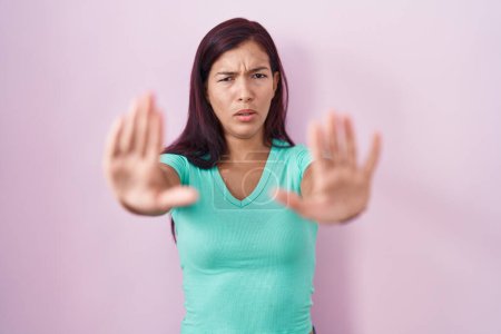 Téléchargez les photos : Young hispanic woman standing over pink background doing stop gesture with hands palms, angry and frustration expression - en image libre de droit