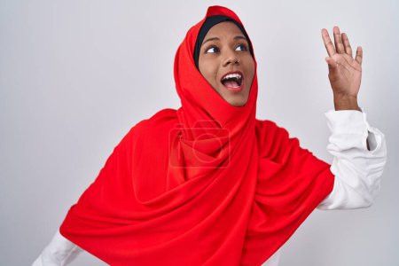 Foto de Mujer árabe joven vistiendo tradicional bufanda islámica hijab bailando feliz y alegre, sonriente movimiento casual y seguro escuchando música - Imagen libre de derechos