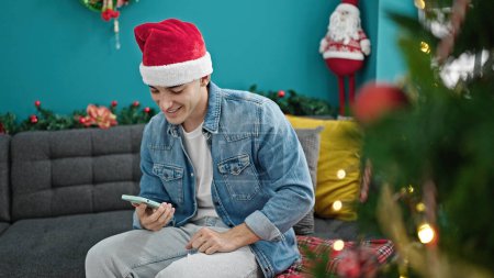 Téléchargez les photos : Jeune homme hispanique utilisant smartphone célébrant Noël à la maison - en image libre de droit