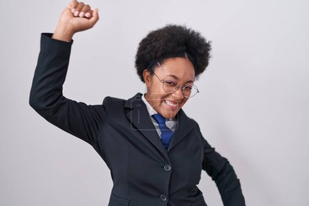 Photo for Beautiful african woman with curly hair wearing business jacket and glasses dancing happy and cheerful, smiling moving casual and confident listening to music - Royalty Free Image