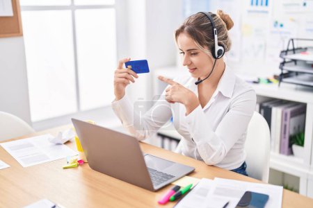 Téléchargez les photos : Jeune femme blonde agent du centre d'appels détenant une carte de crédit travaillant au bureau - en image libre de droit