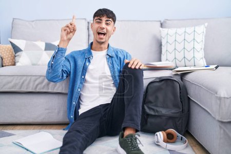 Photo for Young hispanic man sitting on the floor studying for university pointing finger up with successful idea. exited and happy. number one. - Royalty Free Image