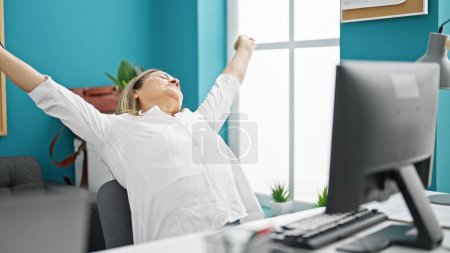 Téléchargez les photos : Moyen Age hispanique femme ouvrière utilisant l'ordinateur fatigué étirement des bras au bureau - en image libre de droit