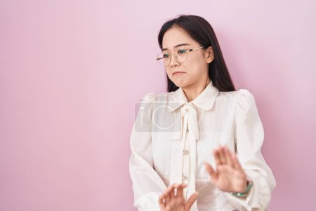 Téléchargez les photos : Jeune femme chinoise debout sur fond rose expression dégoûtée, mécontente et effrayée faisant visage dégoûtant parce que réaction d'aversion. les mains levées - en image libre de droit