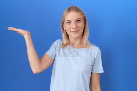 Photo for Young caucasian woman wearing casual blue t shirt smiling cheerful presenting and pointing with palm of hand looking at the camera. - Royalty Free Image