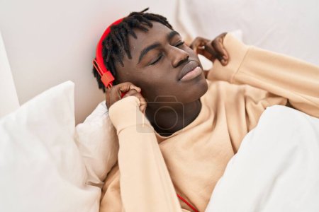 Photo for African american man listening to music lying on bed at bedroom - Royalty Free Image