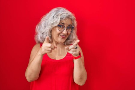 Téléchargez les photos : Femme d'âge moyen avec des cheveux gris debout sur fond rouge pointant les doigts vers la caméra avec un visage heureux et drôle. bonne énergie et vibes. - en image libre de droit