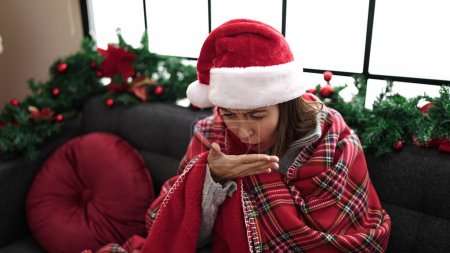 Photo for Young beautiful hispanic woman feeling cold covered with blanket coughing sitting by christmas decoration at home - Royalty Free Image