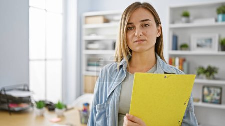Photo for Confident, successful and elegant young blonde business worker radiates positivity while holding a folder at the officeshowcasing the joy of professional success in her relaxed yet concentrated look - Royalty Free Image
