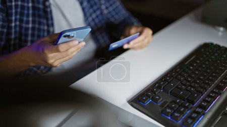 Photo for In the heat of the game, man streamer's hands swiftly wielding smartphone, credit card amid gaming stream in room, balancing virtual entertainment and finance. - Royalty Free Image