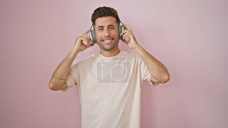 Foto de Joven hispano escuchando música sonriendo sobre un fondo rosa aislado - Imagen libre de derechos