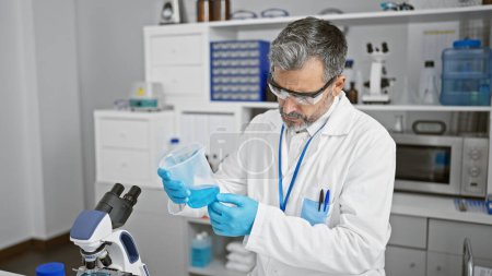 Foto de Un joven hispano concentrado, de pelo gris y guapo, midiendo meticulosamente el líquido para un experimento crítico dentro del bullicioso laboratorio de ciencias - Imagen libre de derechos