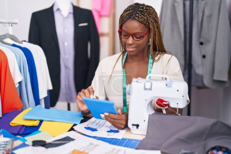 Téléchargez les photos : Femme afro-américaine tailleur souriant confiant en utilisant le pavé tactile au magasin de tailleur - en image libre de droit