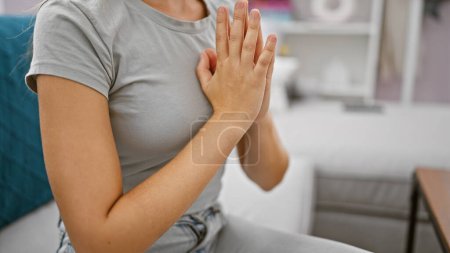 Photo for Woman of faith, relaxed hands praying in comfortable, cozy living room, sitting on sofa at home - an intimate moment of spiritual connection and hope - Royalty Free Image