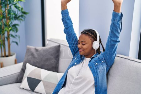 Téléchargez les photos : Femme afro-américaine dansant et écoutant de la musique assise sur le canapé à la maison - en image libre de droit
