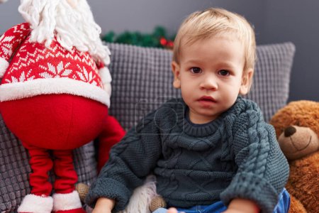 Photo for Adorable blond toddler sitting on sofa by christmas decoration at home - Royalty Free Image
