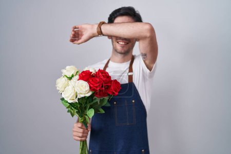 Téléchargez les photos : Jeune homme hispanique tenant bouquet de roses blanches et rouges souriant joyeux jeu jeter un coup d'oeil un boo avec les mains montrant le visage. surpris et sortis - en image libre de droit