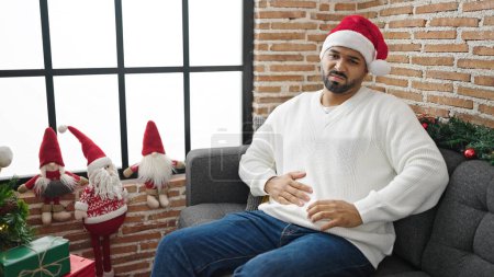 Téléchargez les photos : Homme afro-américain souffrant de maux d'estomac portant un chapeau de Noël à la maison - en image libre de droit