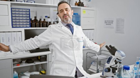 Photo for Tired middle age man, grey haired scientist in lab, stretching over microscope in weary, late-night analysis session. - Royalty Free Image