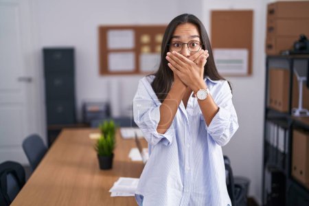 Foto de La joven mujer hispana en la oficina sorprendió cubriendo la boca con las manos por error. concepto secreto. - Imagen libre de derechos