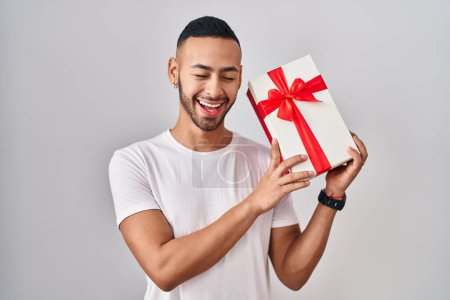 Photo for Young hispanic man holding presents smiling and laughing hard out loud because funny crazy joke. - Royalty Free Image