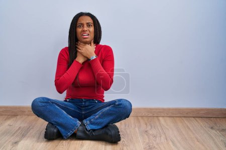 Téléchargez les photos : Jeune afro-américain avec des tresses assises sur le sol à la maison en criant suffoquer parce que l'étranglement douloureux. problème de santé. concept d'asphyxie et de suicide. - en image libre de droit