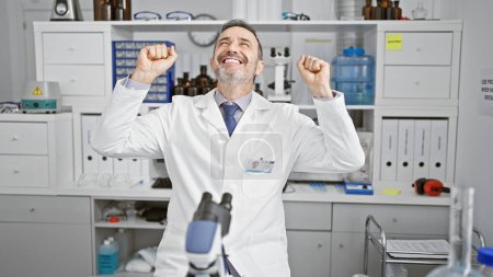 Foto de Feliz hombre de mediana edad con el pelo gris, celebrando un avance científico en su laboratorio - un científico varón seguro de sí mismo utilizando la tecnología de microscopio en el trabajo - Imagen libre de derechos
