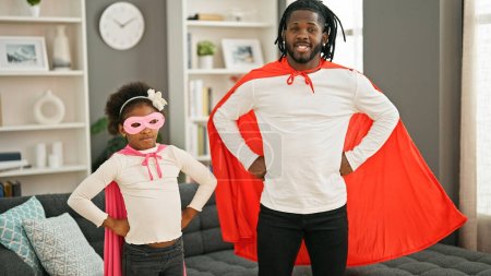 Foto de Padre e hija afroamericanos sonriendo confiados vistiendo traje de superhéroe de pie en casa - Imagen libre de derechos