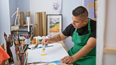 Photo for Passionate young latin artist, diligently immersed in his drawing lesson in art studio, crafting his masterpiece with a paintbrush on a notebook - Royalty Free Image