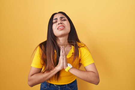 Téléchargez les photos : Jeune femme arabe debout sur fond jaune mendier et prier avec les mains ainsi que l'expression de l'espoir sur le visage très émotionnel et inquiet. mendier. - en image libre de droit