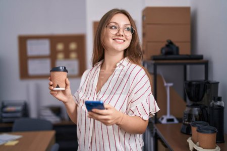 Téléchargez les photos : Jeune femme blonde ouvrière utilisant un smartphone buvant du café au bureau - en image libre de droit