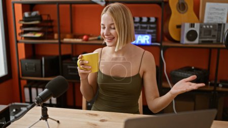 Téléchargez les photos : Jeune femme blonde journaliste radio boire du café parlant au studio de podcast - en image libre de droit