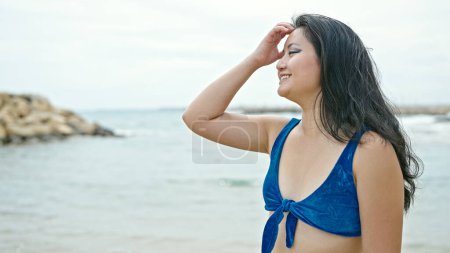 Foto de Joven turista china con bikini peinándose el pelo sonriendo en la playa - Imagen libre de derechos
