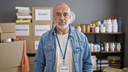 A mature man with a volunteer badge standing in a storage room filled with boxes and supplies.