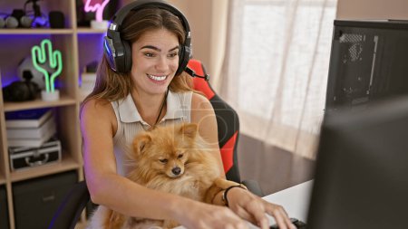 Photo for Young hispanic woman, a radiant dog loving streamer, confidently streams game on computer while playing in night-lit home gaming room - Royalty Free Image