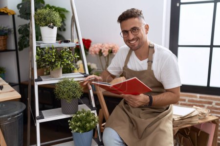Téléchargez les photos : Jeune homme hispanique fleuriste lecture carnet à la boutique de fleurs - en image libre de droit