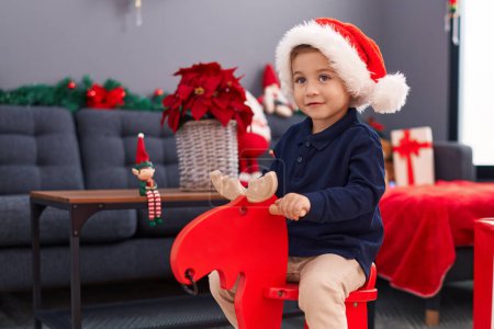 Photo for Adorable hispanic boy playing with reindeer rocking by christmas tree at home - Royalty Free Image