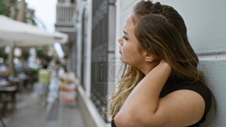 Photo for Concerned young hispanic woman, an urban street portrait of her leaning on wall, thoughtfully doubting under sunny outdoors - Royalty Free Image
