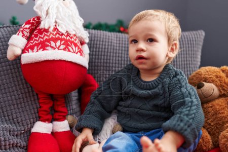 Foto de Adorable niño rubio sentado en el sofá por la decoración de Navidad en casa - Imagen libre de derechos