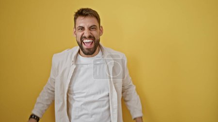 Photo for Angry young hispanic man screaming in frustration, loud fury captured in an isolated portrait, standing against a yellow background expressing serious unhappiness - Royalty Free Image