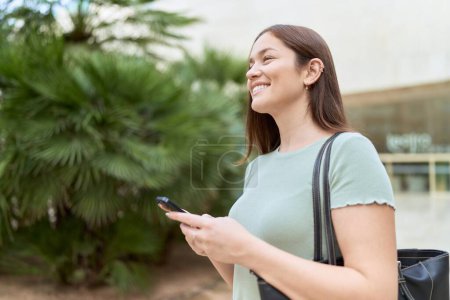 Téléchargez les photos : Jeune belle femme souriant confiant en utilisant smartphone au parc - en image libre de droit