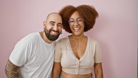 Photo for Happy, confident interracial couple in casual clothes, lovingly standing together with radiant smiles, projecting joy and positive lifestyle, isolated over a beautiful pink background wall. - Royalty Free Image