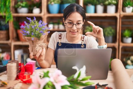 Photo for Young hispanic woman working at florist shop doing video call smiling and confident gesturing with hand doing small size sign with fingers looking and the camera. measure concept. - Royalty Free Image