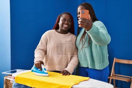 Photo for African american women ironing clothes make selfie by smartphone at laundry room - Royalty Free Image