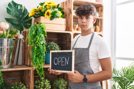 Photo for Hispanic teenager working at florist holding open sign thinking attitude and sober expression looking self confident - Royalty Free Image