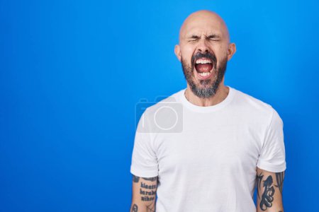 Téléchargez les photos : Homme hispanique avec des tatouages debout sur fond bleu en colère et fou hurlant frustré et furieux, criant de colère. rage et concept agressif. - en image libre de droit